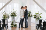 Two grooms sharing their first kiss at the altar at The Point at Pier 70 wedding with pedestal floral arrangements and elegant draping in the background.