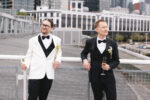 Grooms sharing a quiet moment on the balcony at The Point at Pier 70 with the Seattle skyline in the background of their wedding venue.