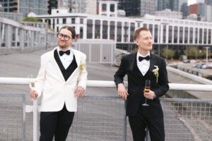 Grooms sharing a quiet moment on the balcony at The Point at Pier 70 with the Seattle skyline in the background of their wedding venue.