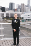 Groom posing for an editorial solo wedding photography portrait in a black tuxedo with the Seattle skyline in the background