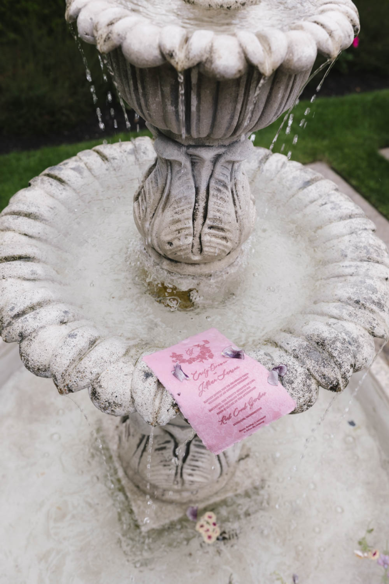 Wedding stationery floating on various tiers of a three-tier stone fountain at Rock Creek Gardens